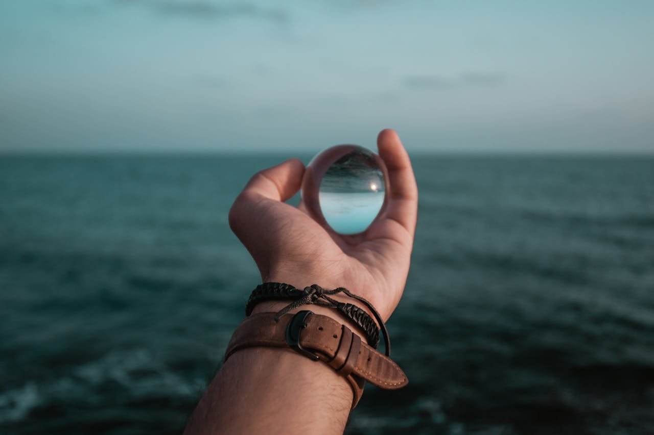 Person Holding Glass Marble Infront of Sea